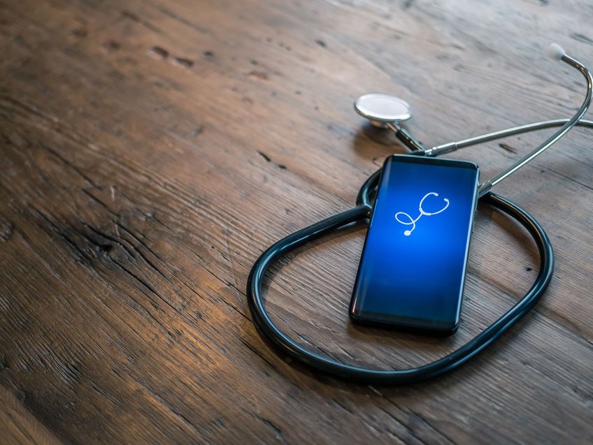 Mobile phone with healthcare app on wood table with stethoscope